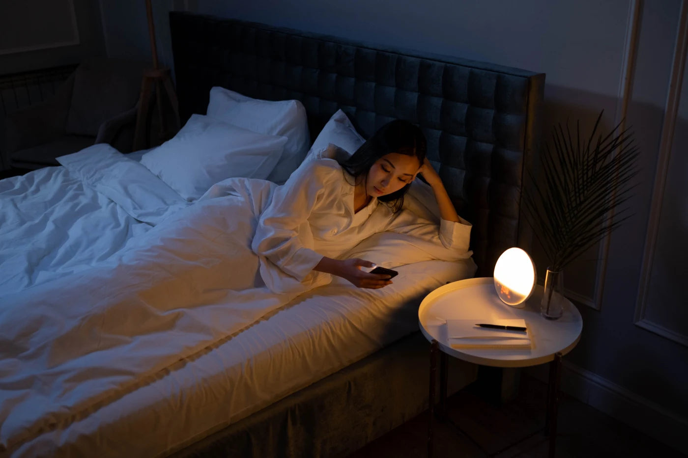 A woman awake in bed looking at her phone
